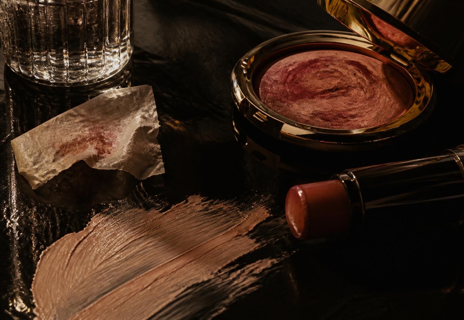 Dark editorial still life of cream pigment, a gold compact and a spent blotting paper